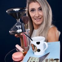 Valeria regge in mano una clessidra e un vassoio con un caffè, un macaron, un libro e dei cosmetici